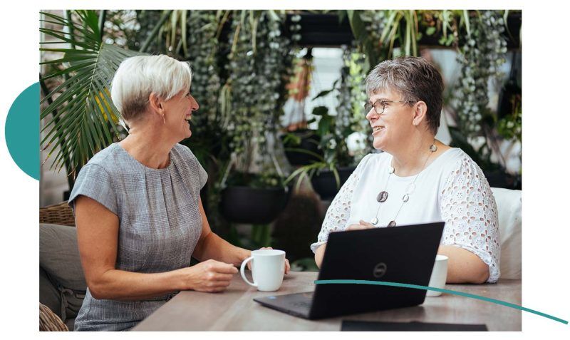 Jodie Simpson working with a client, a laptop sits on the table and two coffee mugs.